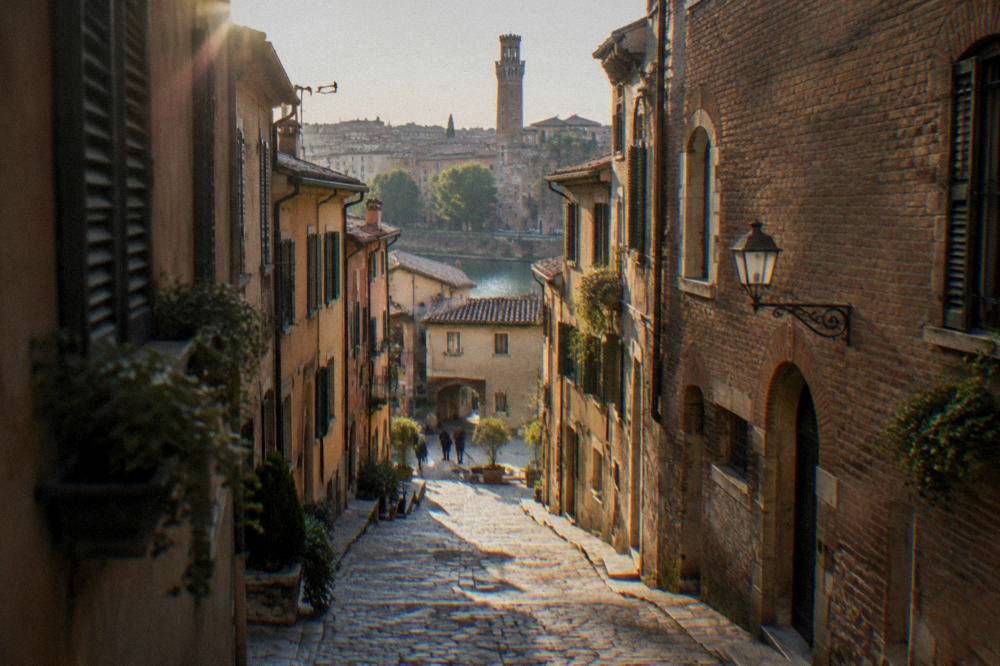 Narrow cobbled street in Verona's old town with brick facades and a distant tower