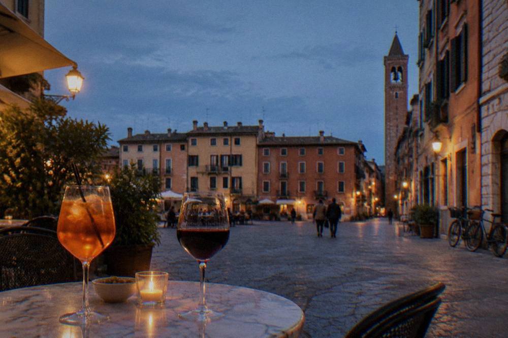 Glasses of orange spritz and red wine on a marble table in a lamplit square