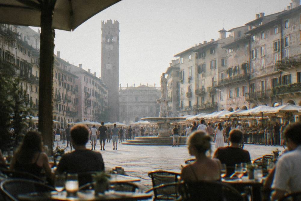 Evening crowd with drinks at outdoor tables in Piazza delle Erbe under historic facades