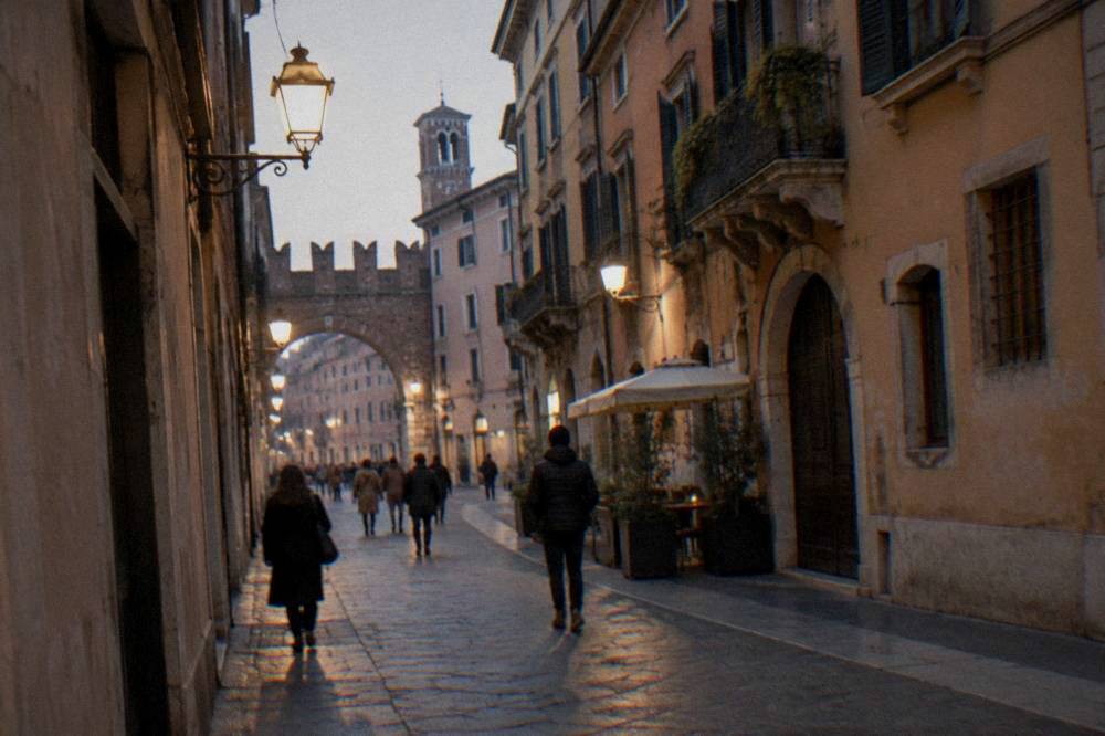 People strolling in a lamplit medieval street of Verona in the evening