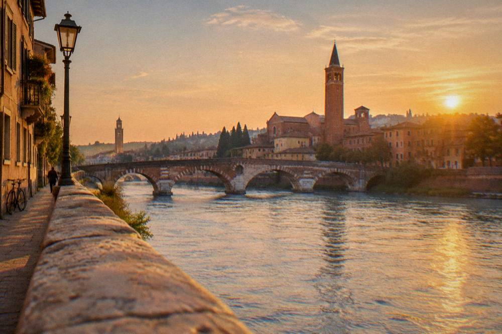 Evening view from a riverside spot over the Adige with Verona's bridges and towers lit