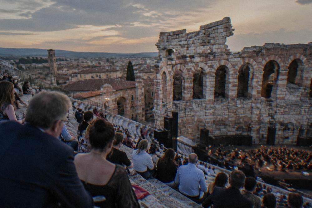 Opera audience members seated on the stone steps of the Arena of Verona at twilight