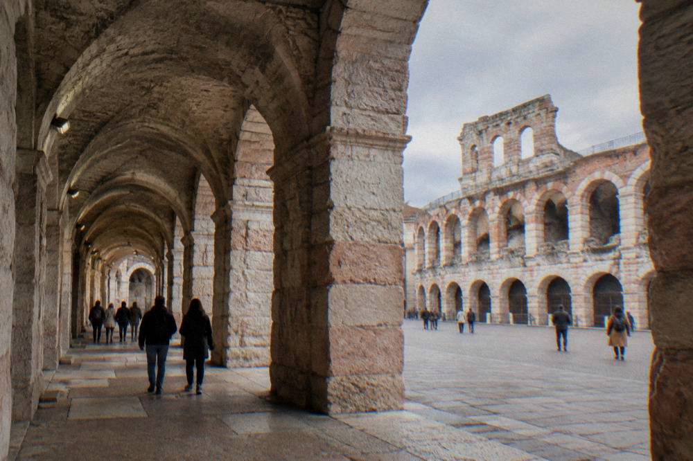 The interior arcades of the Arena of Verona in daylight, with visitors walking through the stone vaults