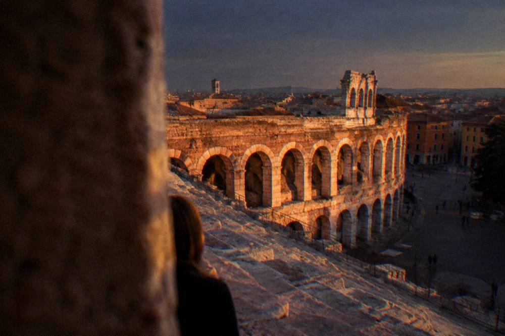 The stone steps and arches of the Arena of Verona seen from an upper row under a dark evening sky