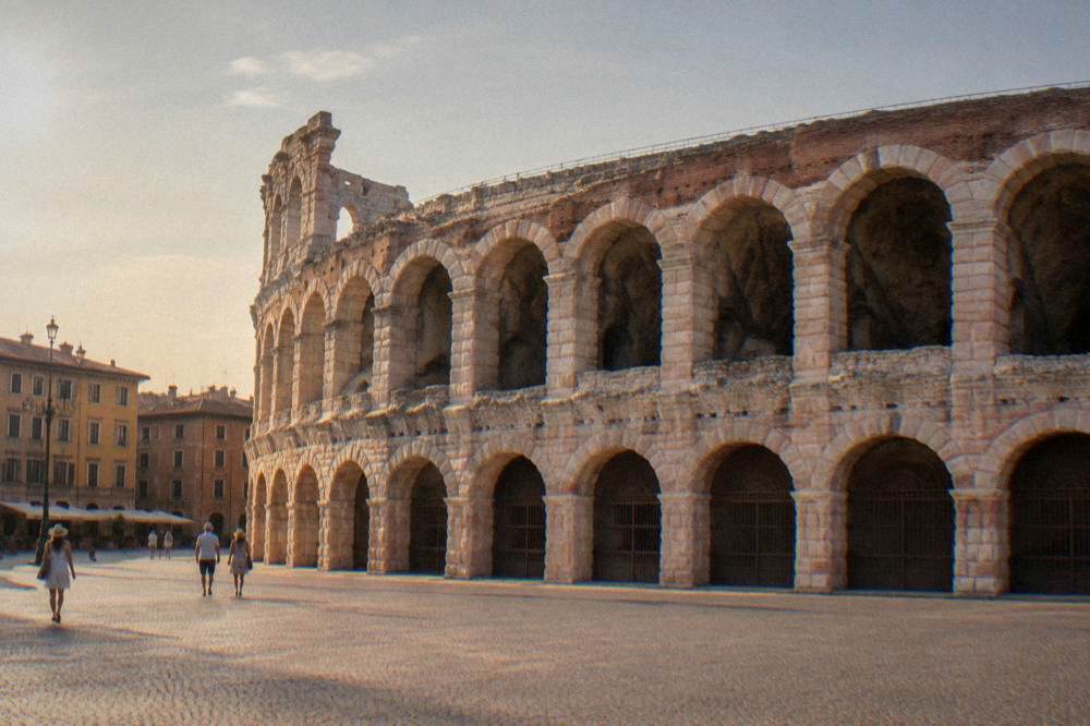 Roman amphitheatre lit warmly at dusk with an empty square in front