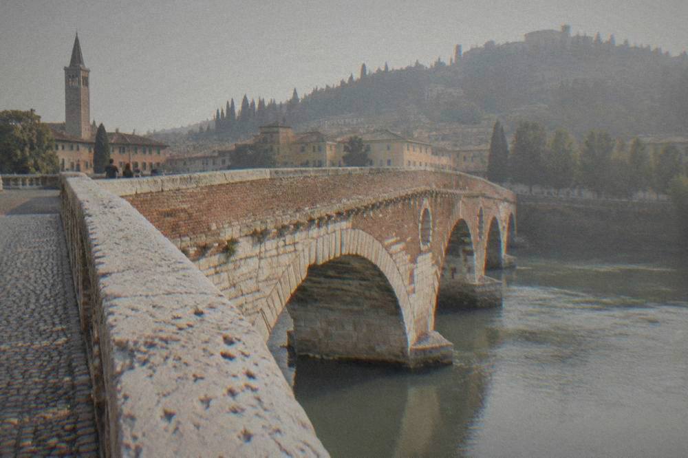 Close view of the worn stone arches and white cobbles of Ponte Pietra in early light