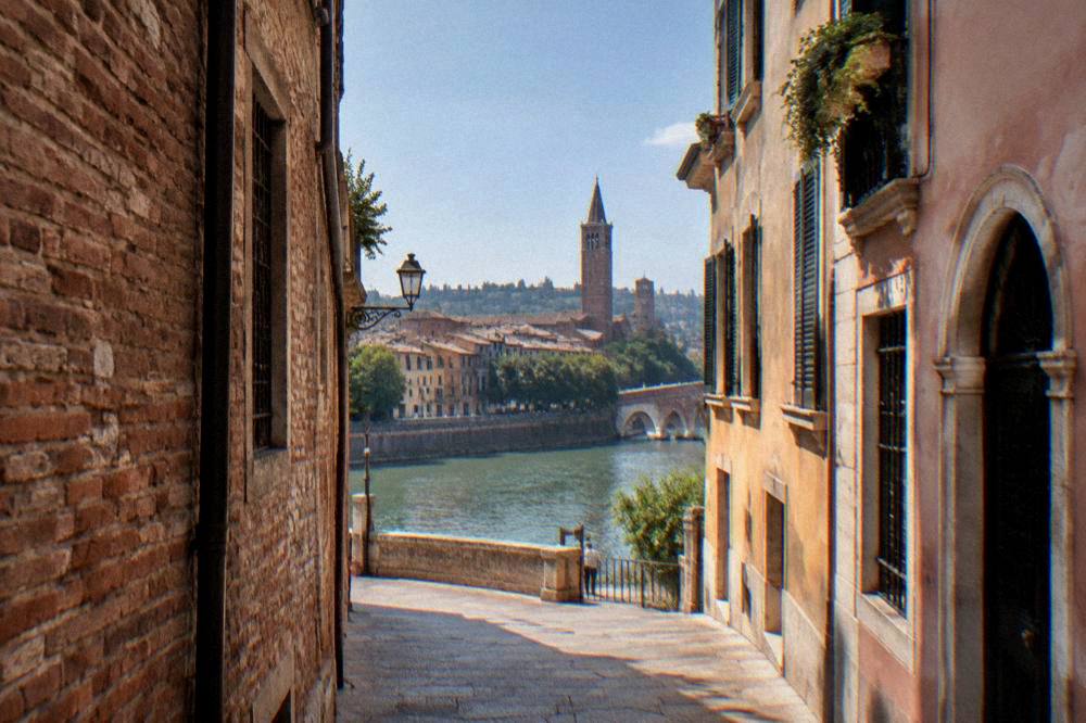 A walker's view down a narrow Verona lane of brick and stone toward the Adige river