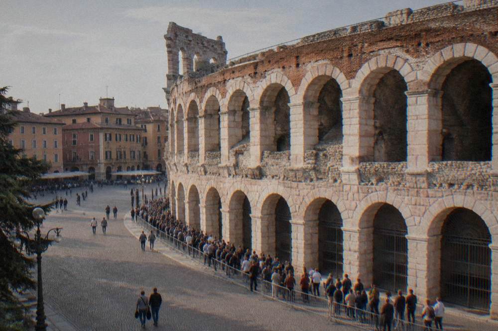 A ticket queue outside the Arena di Verona with visitors waiting in late afternoon sun along the arches