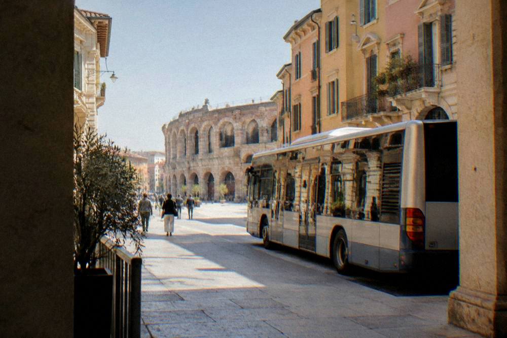 A city bus stopped on a street in Verona with the Arena visible in the background