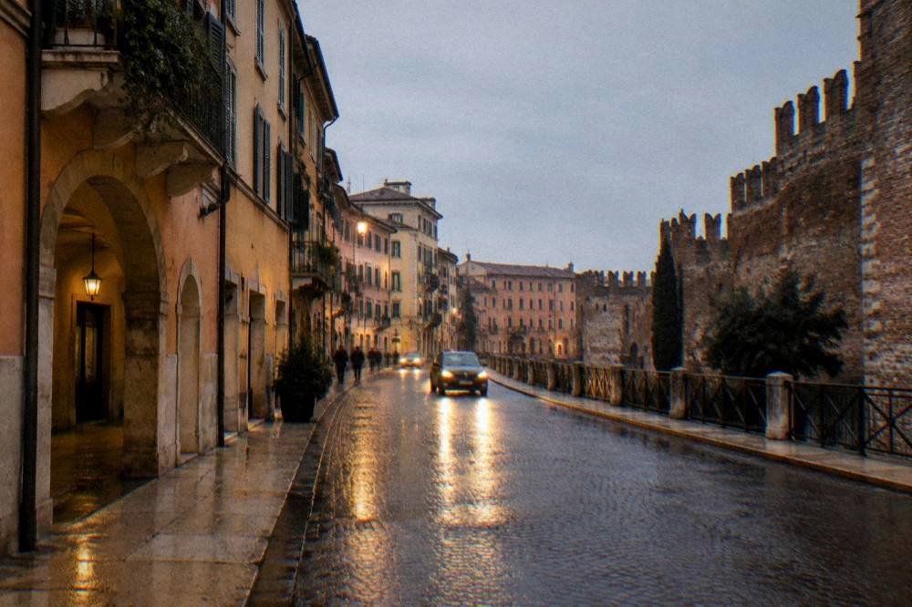 A wet evening street in Verona with headlights reflecting on cobblestones near the old city walls