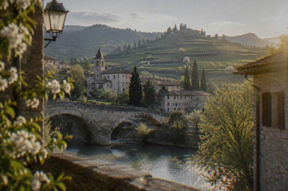 Historic city street with stone buildings and a stone bridge over a river at dusk