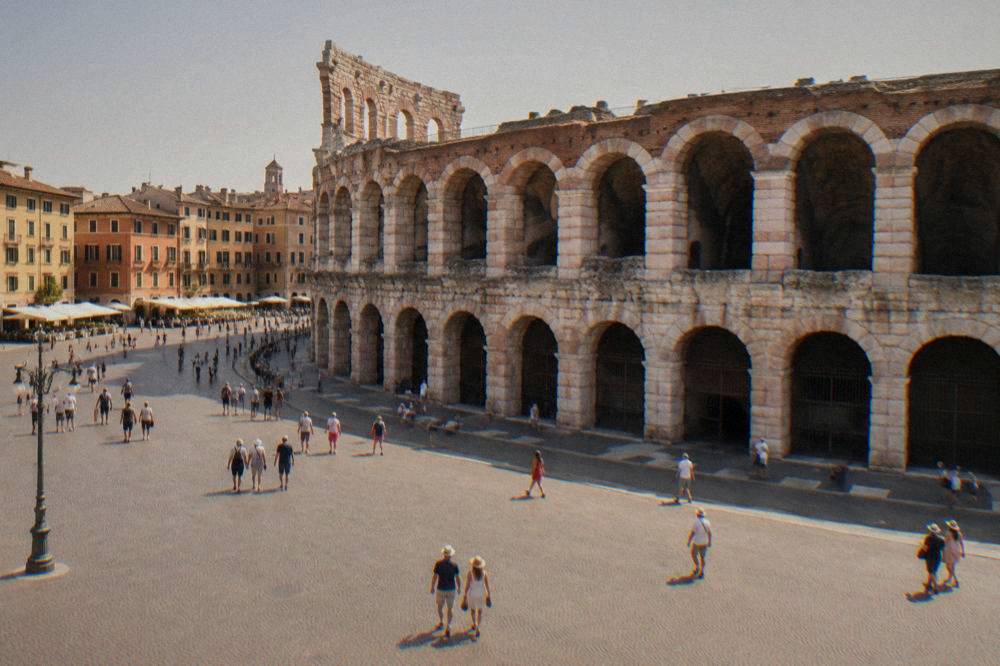 Lit Roman amphitheatre facade seen from a wide paved square at dusk