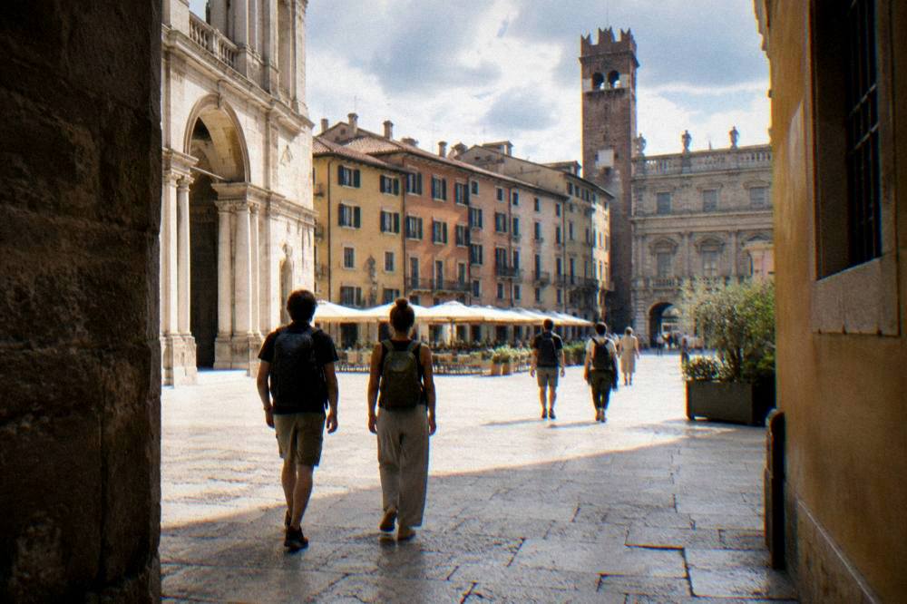 Travellers with backpacks walking through a sunlit Verona piazza