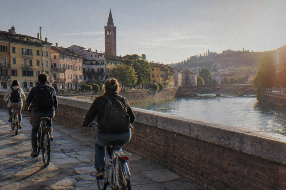A small group of cyclists crossing a bridge over the Adige river in Verona