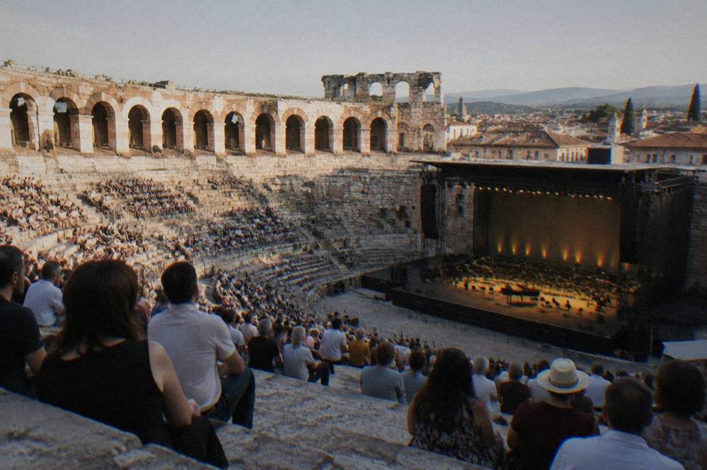 Audience seated on the stone steps of the Verona Arena before an evening opera performance