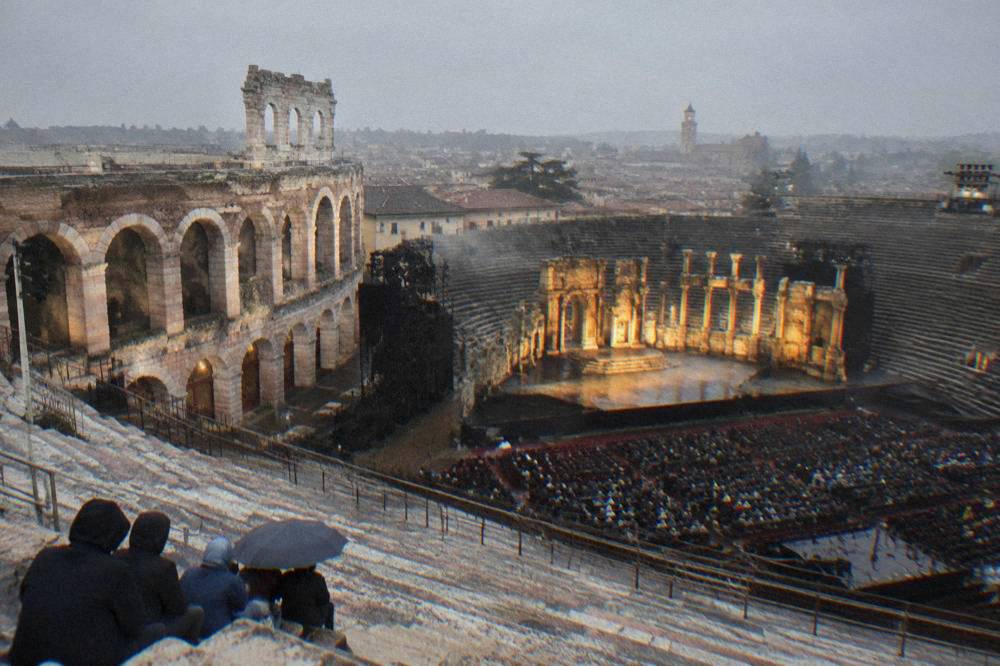 Lit stage inside the Verona Arena seen from upper stone seating before a performance