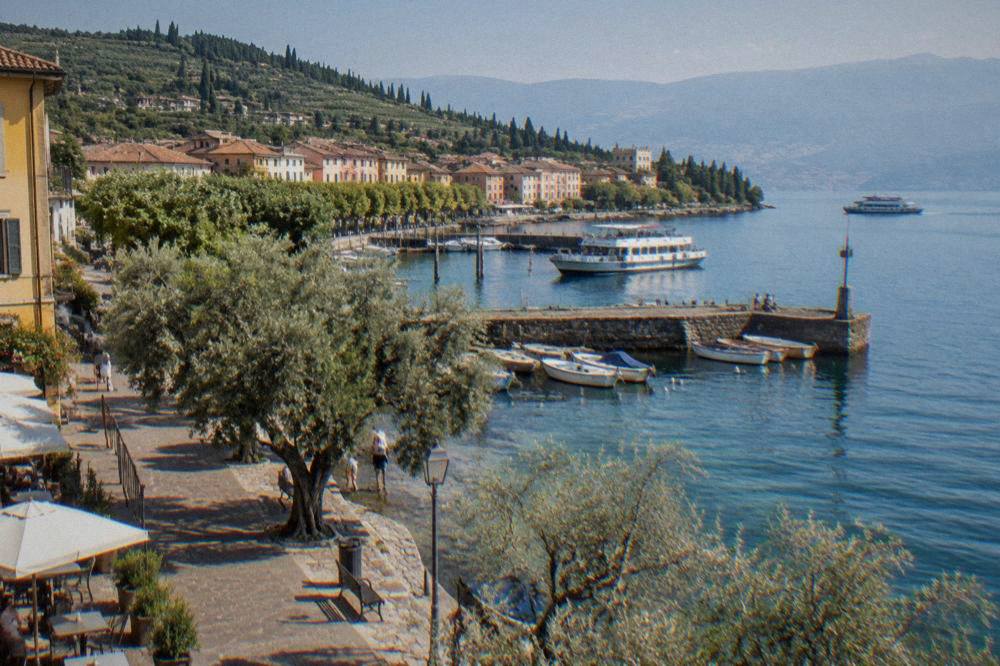 A lakeside promenade with olive trees and ferries at Bardolino