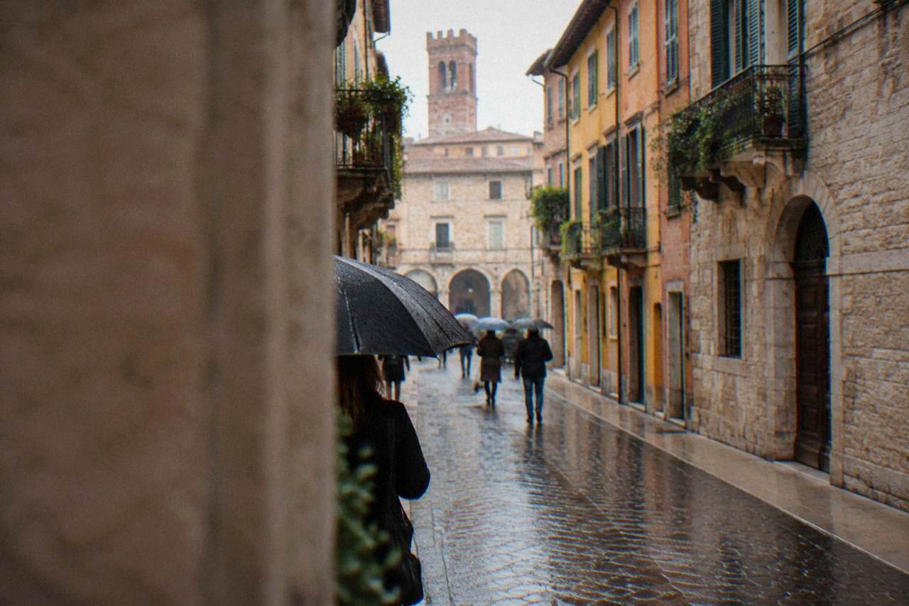 Wet cobblestone street in Verona with rain-slicked stone buildings and umbrellas
