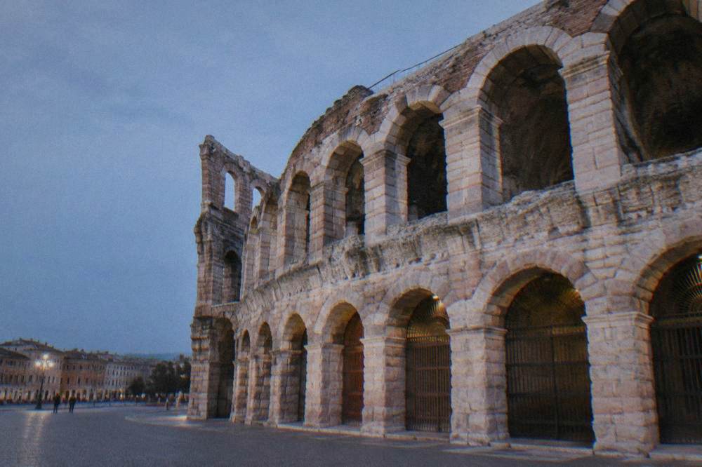 Interior of the Verona Arena on a grey day, empty stone seating tiers rising around the stage area
