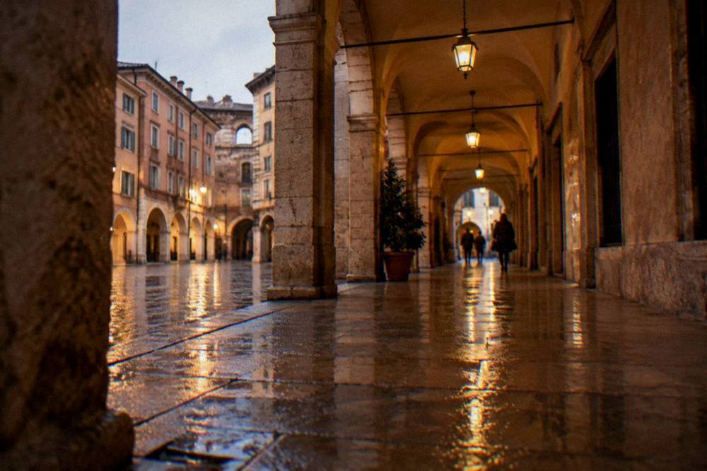 Evening view of a lamplit covered arcade in Verona with wet paving reflecting the light