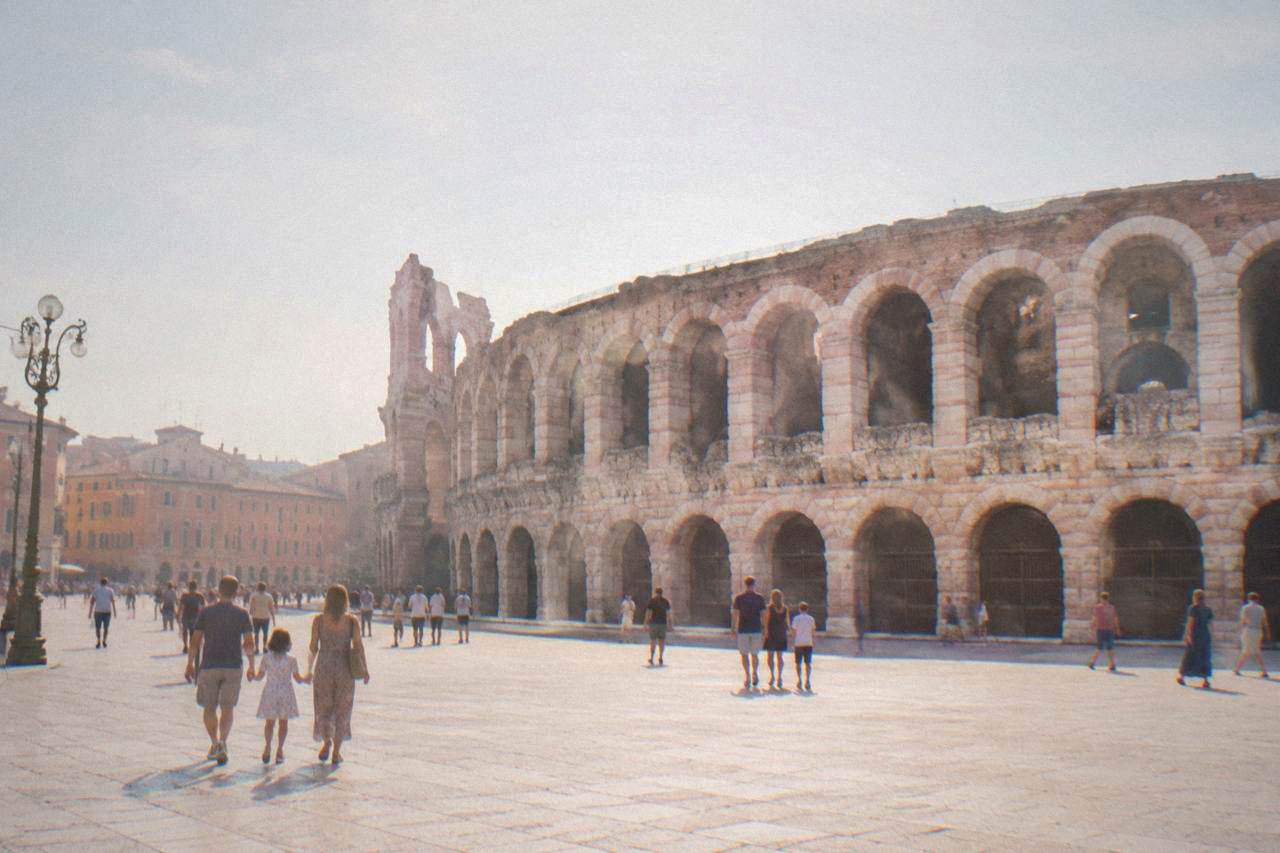 Families walking across a wide marble square in Verona with the Roman Arena wall behind them