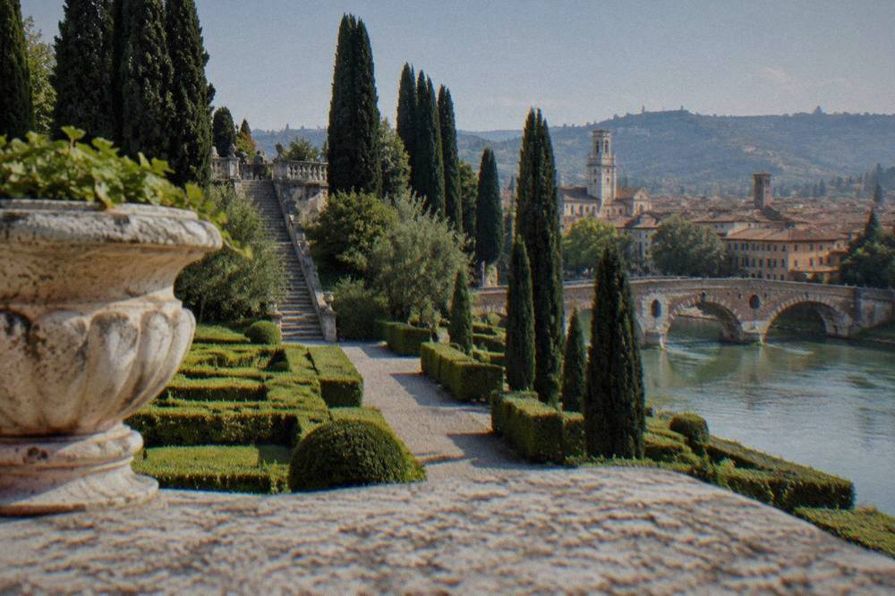 A stone Roman bridge arching over the green Adige river with hills behind