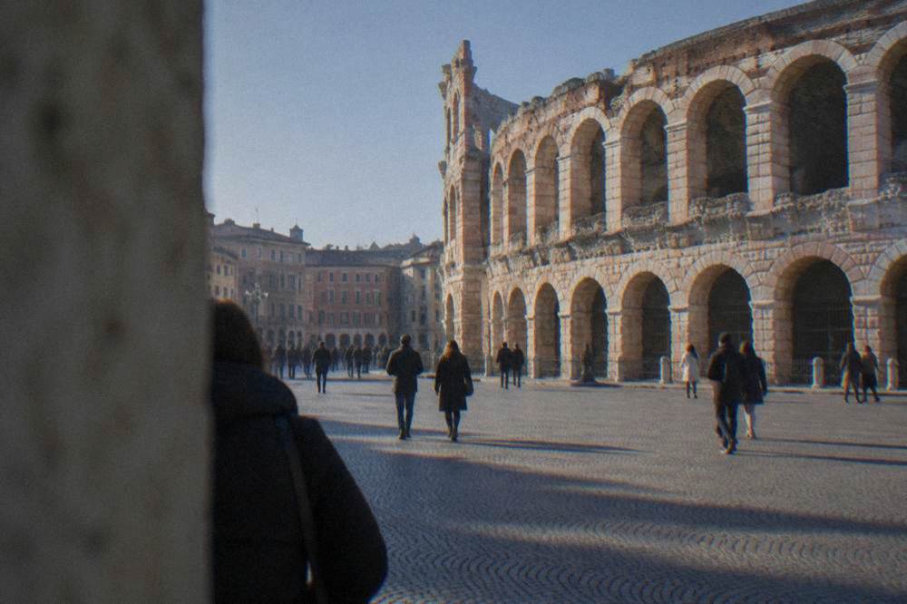 People walking across Piazza Bra in Verona under a clear blue sky with the Arena at the edge